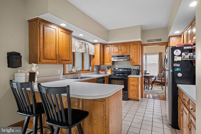 kitchen featuring under cabinet range hood, light countertops, a peninsula, black appliances, and a sink