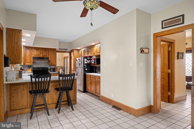 kitchen with black range with electric stovetop, a ceiling fan, under cabinet range hood, freestanding refrigerator, and light tile patterned floors