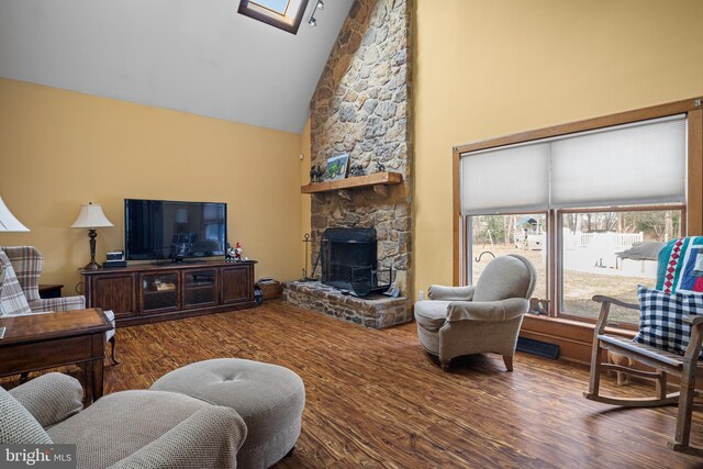 living area with a wood stove, wood finished floors, and high vaulted ceiling