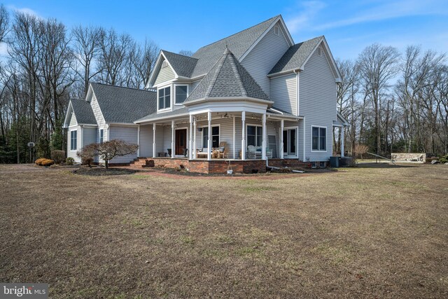 victorian-style house featuring central air condition unit, covered porch, a shingled roof, and a front yard