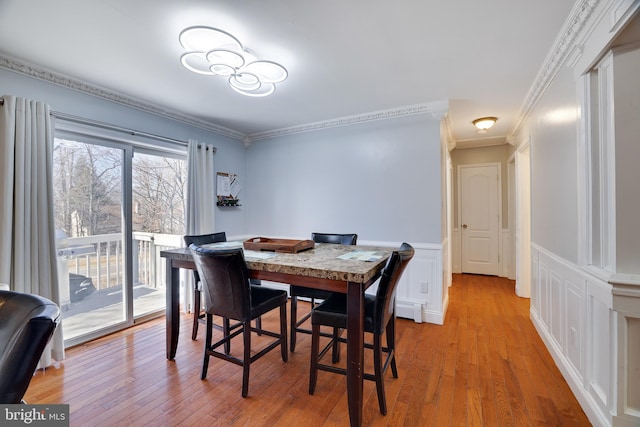 dining room with a wainscoted wall, light wood-style flooring, crown molding, and a decorative wall