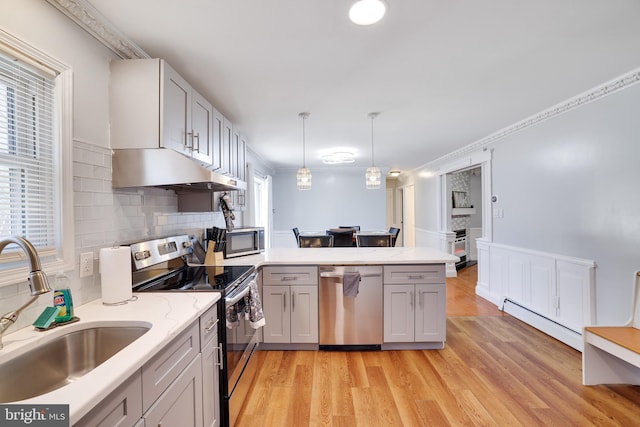 kitchen featuring a sink, under cabinet range hood, appliances with stainless steel finishes, a peninsula, and baseboard heating