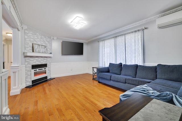 living area with a large fireplace, an AC wall unit, light wood-type flooring, wainscoting, and ornate columns