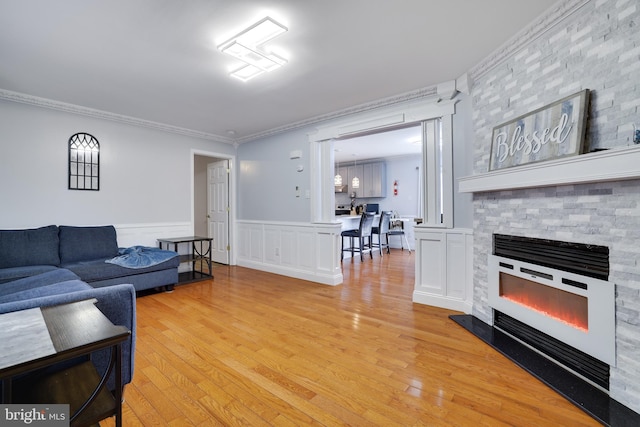 living room featuring light wood finished floors, a stone fireplace, wainscoting, and ornamental molding