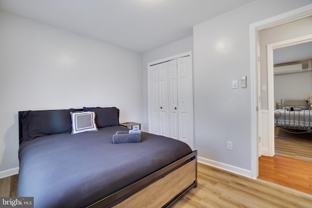 bedroom with a wall mounted air conditioner, a closet, baseboards, and light wood-style floors