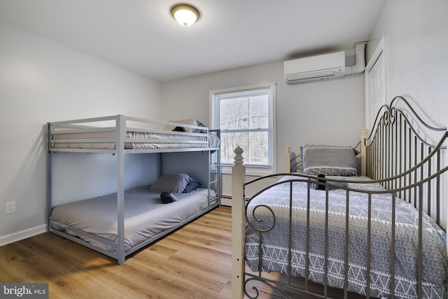 bedroom with a wall mounted AC, baseboards, and wood finished floors