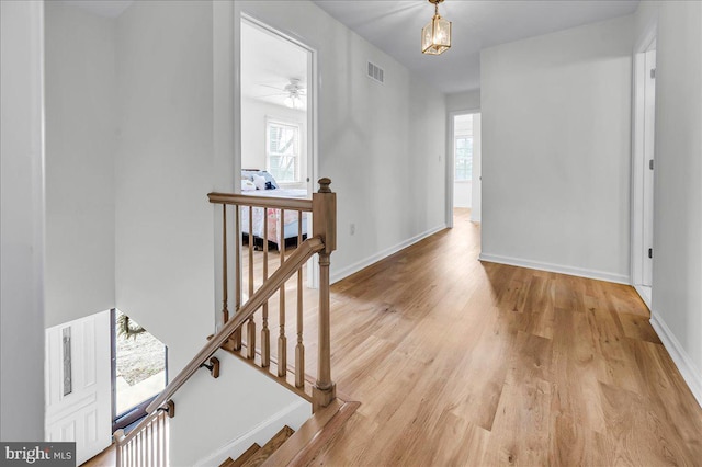 hall with an upstairs landing, visible vents, light wood finished floors, and baseboards