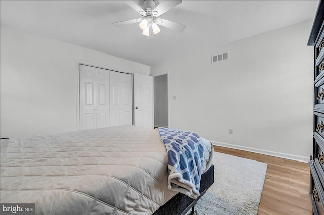 bedroom with visible vents, baseboards, wood finished floors, a closet, and a ceiling fan