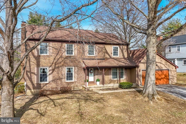 view of front of house featuring brick siding, a front lawn, covered porch, a chimney, and driveway