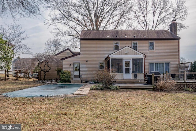 back of property with a deck, a chimney, a yard, and a sunroom