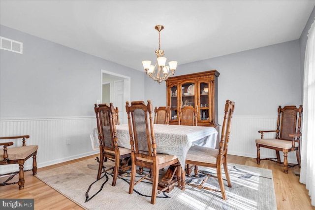 dining room featuring visible vents, light wood-type flooring, an inviting chandelier, and a wainscoted wall