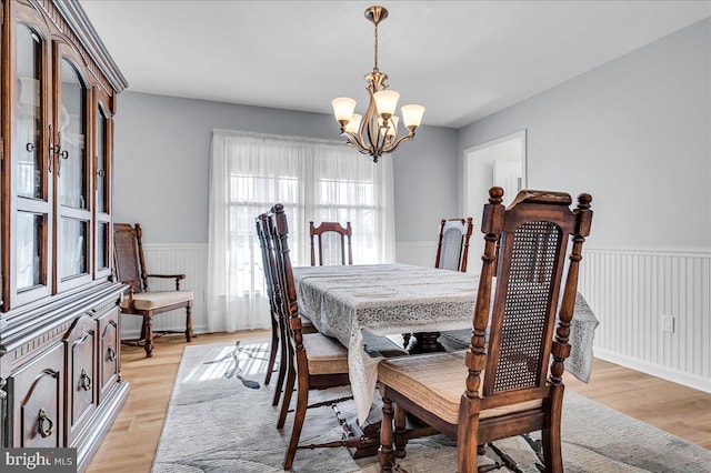 dining area featuring an inviting chandelier, wainscoting, and light wood finished floors