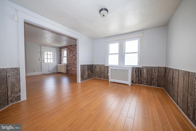 spare room featuring radiator, light wood-style floors, and wainscoting