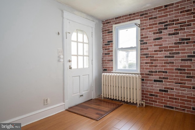 foyer featuring baseboards, brick wall, radiator heating unit, and hardwood / wood-style flooring