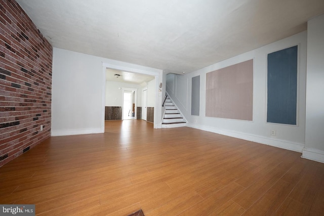 unfurnished living room with brick wall, stairs, and wood finished floors