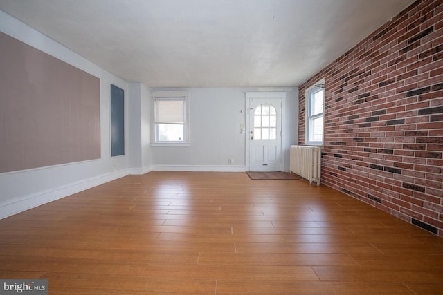 entrance foyer featuring baseboards, brick wall, wood finished floors, and radiator heating unit