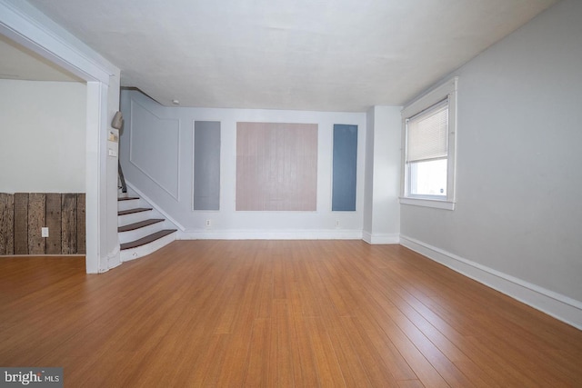 unfurnished living room featuring stairway, baseboards, and light wood-style flooring