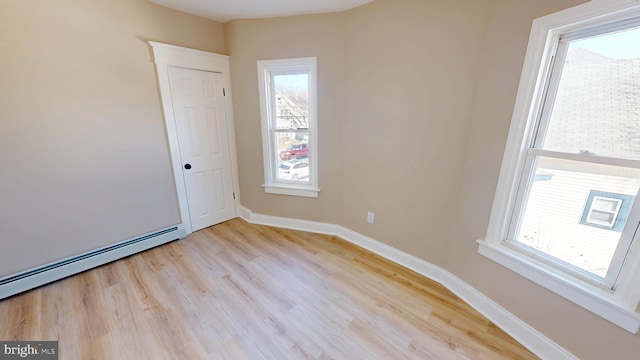 unfurnished room with baseboard heating, light wood-style flooring, and baseboards