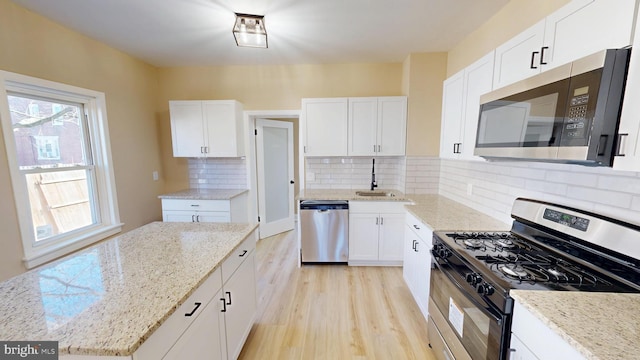 kitchen with white cabinetry, light stone countertops, light wood-style flooring, stainless steel appliances, and a sink