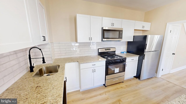 kitchen with a sink, stainless steel appliances, light wood-style floors, and white cabinetry