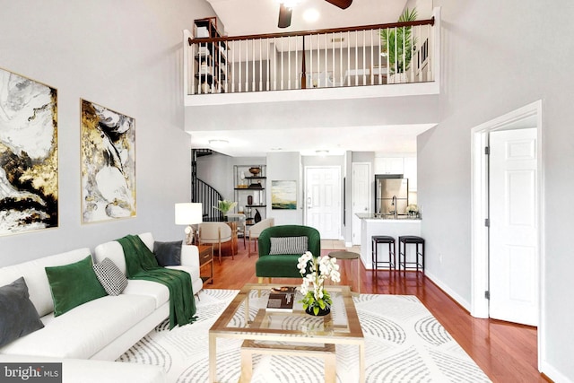 living area featuring a ceiling fan, wood finished floors, baseboards, a towering ceiling, and stairs