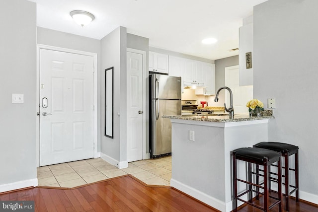 kitchen featuring a peninsula, light wood-style flooring, a sink, white cabinets, and appliances with stainless steel finishes