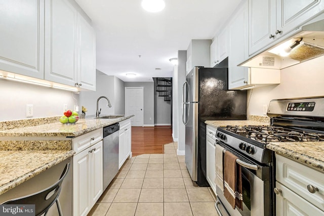 kitchen featuring light tile patterned floors, a sink, stainless steel appliances, under cabinet range hood, and white cabinetry