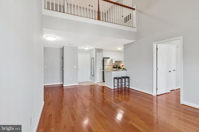 unfurnished living room featuring a high ceiling, baseboards, and light wood-type flooring