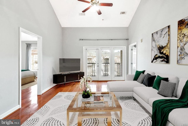 living area with visible vents, baseboards, wood finished floors, high vaulted ceiling, and a ceiling fan