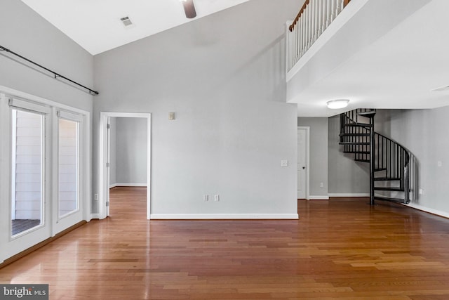 unfurnished living room featuring a high ceiling, stairway, wood finished floors, and visible vents