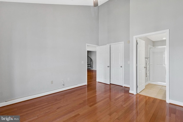 unfurnished bedroom with baseboards, a towering ceiling, ensuite bathroom, and hardwood / wood-style flooring