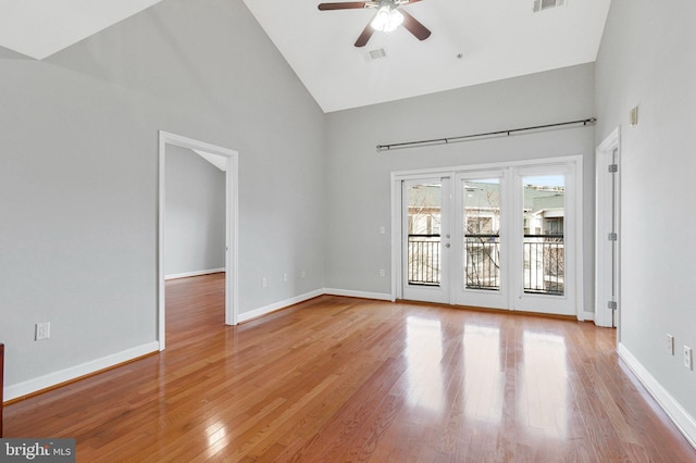 empty room with light wood finished floors, visible vents, high vaulted ceiling, and baseboards