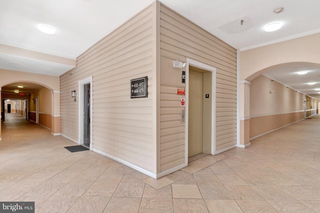 corridor with baseboards, elevator, arched walkways, and wood walls