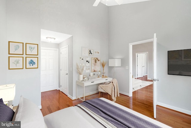 bedroom with a high ceiling, wood finished floors, baseboards, and ceiling fan