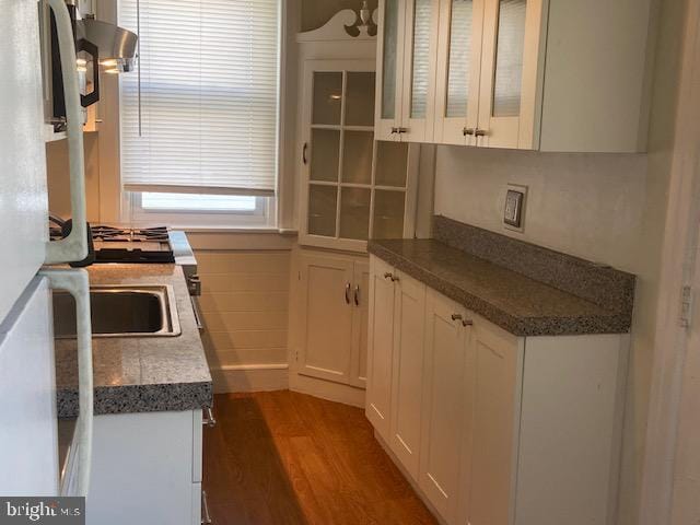 kitchen featuring dark wood-type flooring, cooktop, white cabinets, exhaust hood, and glass insert cabinets