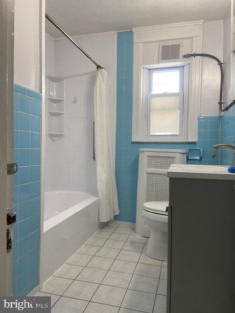 full bathroom with tile patterned floors, visible vents, toilet, and tile walls