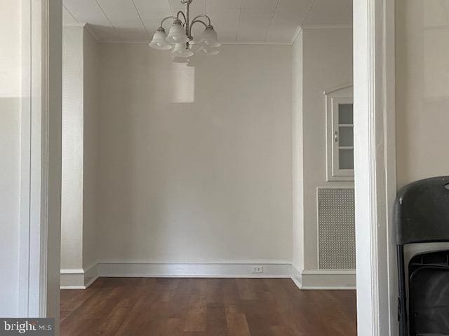 unfurnished dining area featuring dark wood finished floors, crown molding, baseboards, and an inviting chandelier