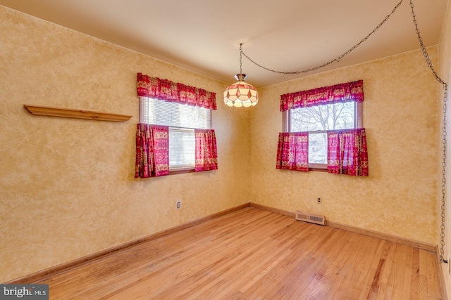 unfurnished room with a healthy amount of sunlight, visible vents, wood-type flooring, and baseboards