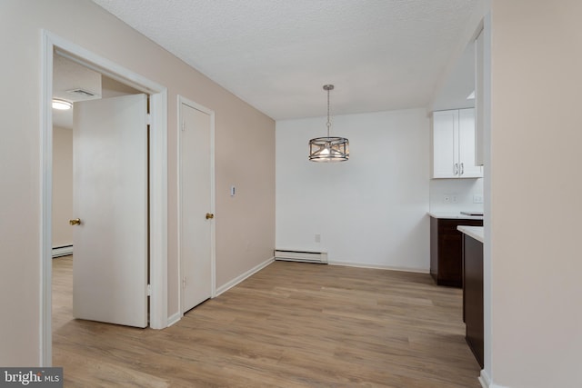 unfurnished dining area with baseboard heating, a textured ceiling, and light wood-style floors