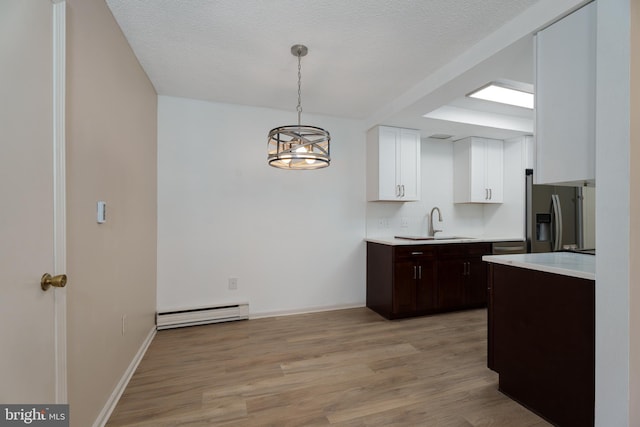 kitchen with a baseboard radiator, stainless steel fridge, white cabinetry, and light countertops