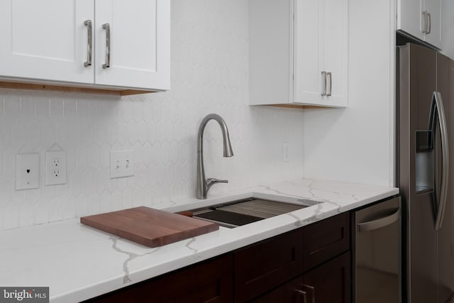 kitchen with a sink, backsplash, white cabinetry, appliances with stainless steel finishes, and light stone countertops