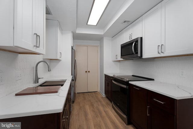 kitchen featuring visible vents, a sink, dark brown cabinetry, appliances with stainless steel finishes, and white cabinets