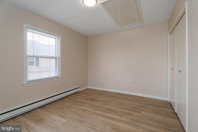 spare room with a baseboard radiator, a textured ceiling, attic access, and light wood-style flooring