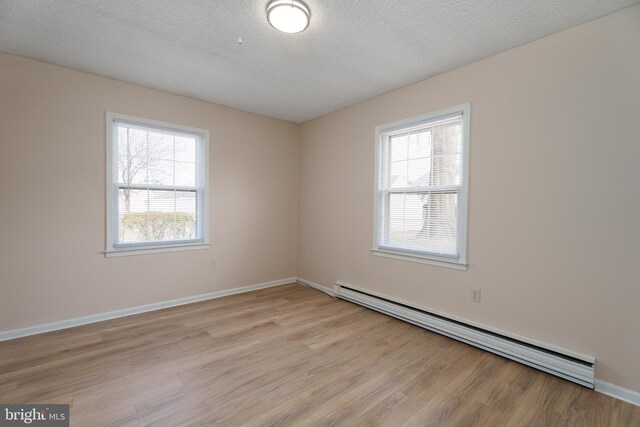 spare room featuring light wood-type flooring, a baseboard radiator, baseboards, and a textured ceiling