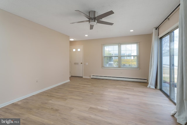 spare room with a baseboard heating unit, plenty of natural light, light wood-style floors, and baseboards