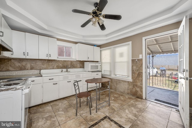 kitchen with white cabinetry, white appliances, tile walls, light countertops, and a raised ceiling