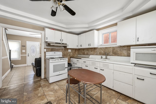 kitchen with white appliances, light countertops, white cabinets, under cabinet range hood, and a raised ceiling