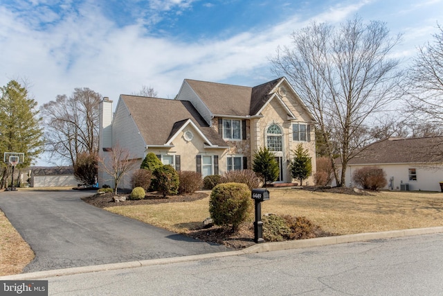 traditional home featuring stone siding, a chimney, a front yard, and a shingled roof