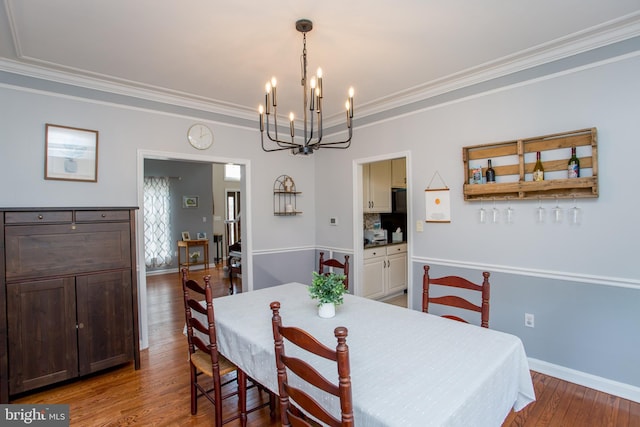 dining area with ornamental molding, wood finished floors, baseboards, and a chandelier