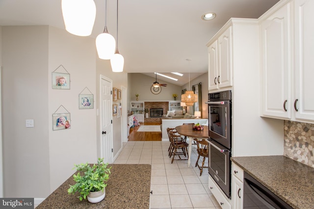 kitchen featuring multiple ovens, a ceiling fan, a fireplace, light tile patterned floors, and vaulted ceiling